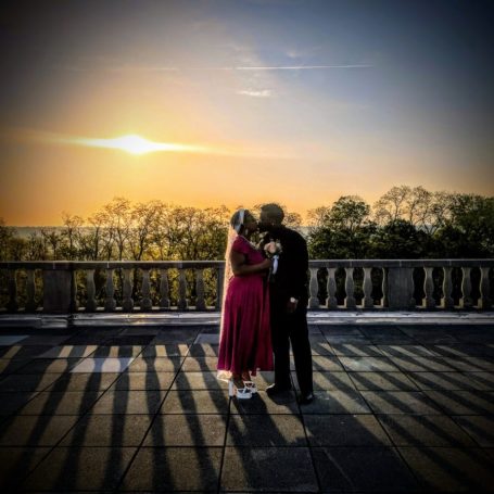 Couple embracing at sunset, with shadows cast on a balcony railing. Personalized Ceremonies.